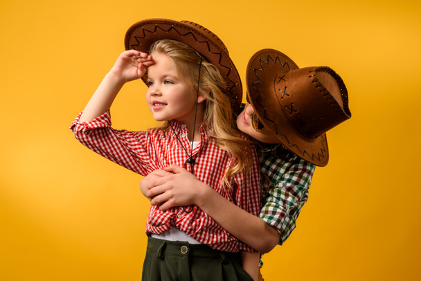 little cowboy embracing stylish cowgirl, isolated on yellow - Foto, imagen