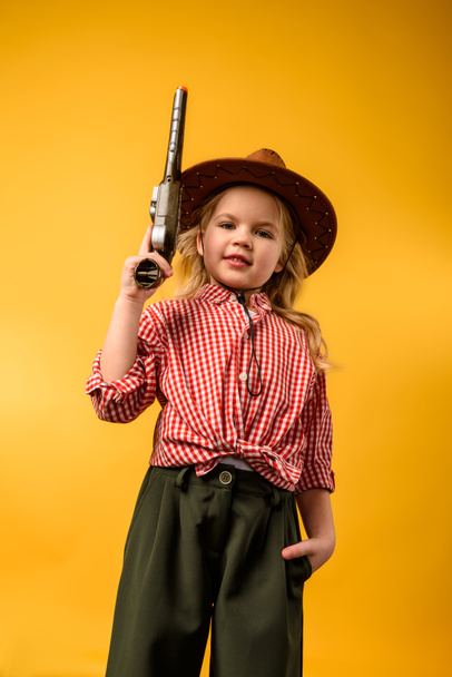 stijlvolle cowgirl in muts met pistool, geïsoleerd op geel - Foto, afbeelding