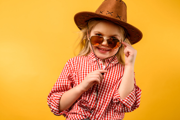 стильная девушка в шляпе и солнцезащитных очках, изолированная на желтом
 - Фото, изображение