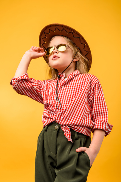 schönes stylisches Cowgirl mit Hut und Sonnenbrille, isoliert auf gelb - Foto, Bild