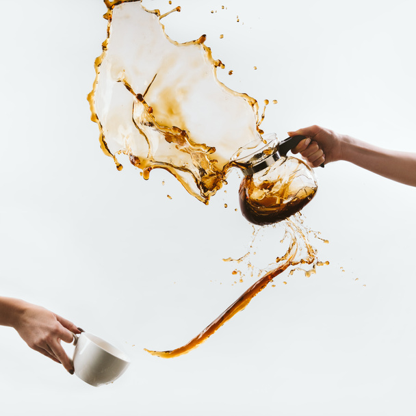 cropped view of hands splashing coffee from cup and glass pot, isolated on white - Foto, afbeelding