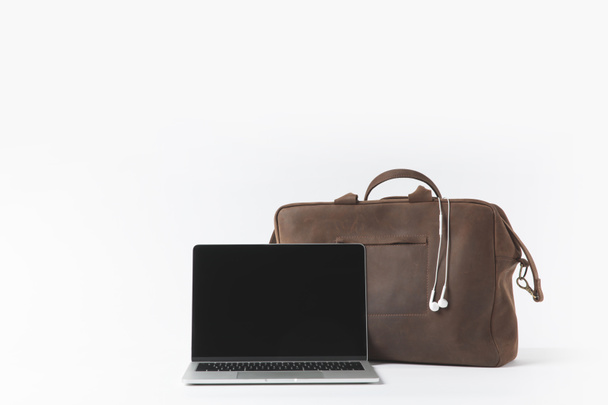 close up view of laptop with blank screen and stylish bag with earphones isolated on white - Photo, Image