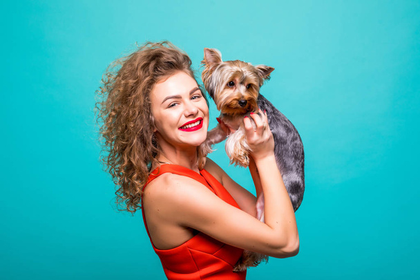 Mädchen mit yorkie Hund. Schönheit junge Mädchen in rotem Kleid umarmen ihre süße yorkshire Terrier isoliert auf grünem Hintergrund - Foto, Bild