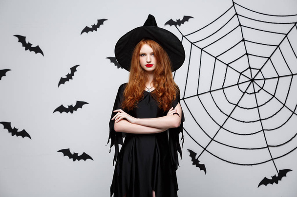 Koncepcja witch halloween - Halloween czarownica trzyma pozowanie z poważną miną nad ciemnym studio szary tło z bat i spider web. - Zdjęcie, obraz