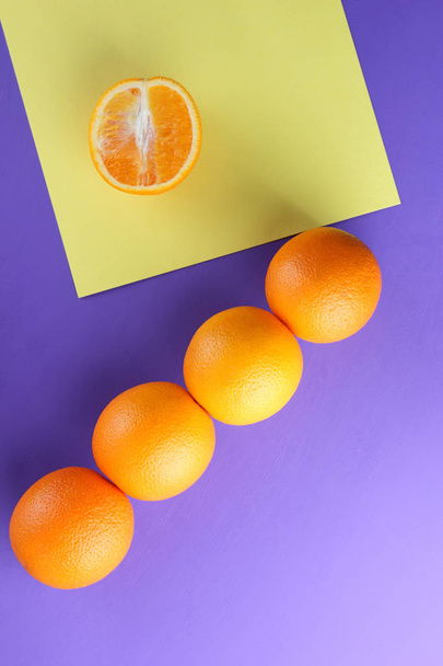 Whole and sliced fruit oranges on a purple background, citrus in pop art style, copy space, a lot of oranges on a colorful background, figures of tropical fruit on a table, ultraviolet - Photo, Image