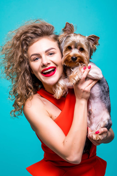 Portrait of smiling young attractive woman looking at camera and holding Yorkshire terrier isolated view on green background. - Photo, Image