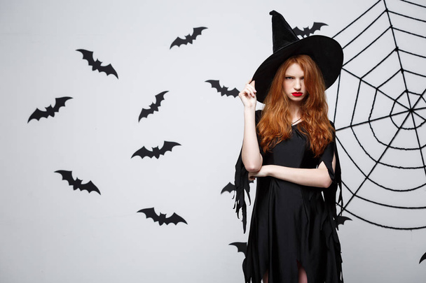 Concept de sorcière d'Halloween - Sorcière d'Halloween posant avec une expression sérieuse sur fond de studio gris foncé avec chauve-souris et toile d'araignée
. - Photo, image