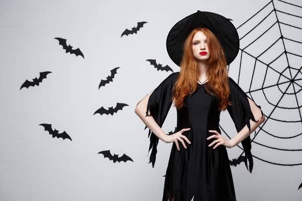 Conceito de bruxa de Halloween - Halloween Witch segurando posando com expressão séria sobre fundo de estúdio cinza escuro com teia de morcego e aranha
. - Foto, Imagem