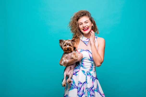 Портрет улыбающейся кудрявой женщины, держащей собаку-терьера изолированной на цветном фоне
 - Фото, изображение