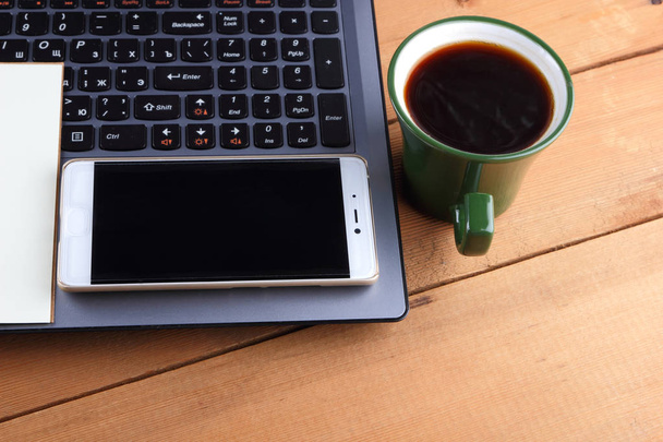 Laptop a šálku kávy na dřevěné pozadí, pracovní stanice na starý stůl, smartphone a notebook, pero a brýle na pracovišti, značkové pracovní stanice, kancelář - Fotografie, Obrázek