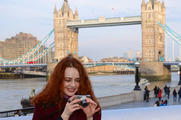 Λονδίνο κορίτσι κοντά στη γέφυρα του Πύργου. Πορτρέτο του όμορφη νεαρή γυναίκα χαμογελαστή στο Λονδίνο. Λονδίνο γυναίκα λαμβάνοντας τουριστική φωτογραφία στο Tower Bridge με κάμερα. Κορίτσι απολαμβάνοντας θέα πάνω από τον ποταμό Τάμεση, στο Λονδίνο. Έννοια του τουρισμού Ηνωμένο Βασίλειο. - Φωτογραφία, εικόνα