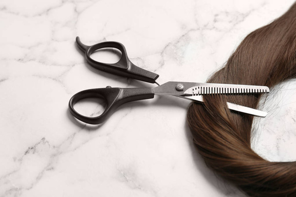 Professional hairdresser scissors and strand of brown hair on marble background - Φωτογραφία, εικόνα