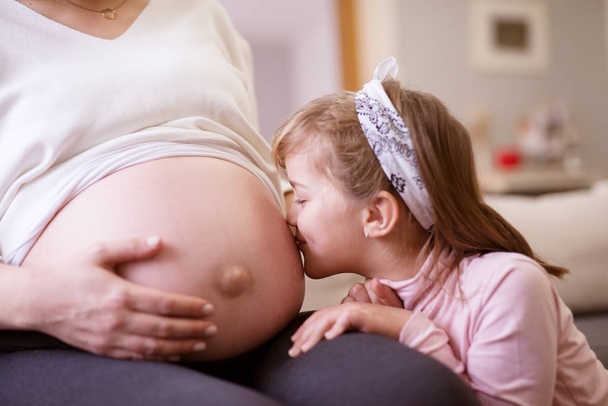 小さな幼児の女の子妊娠中の母親の腹にキス  - 写真・画像