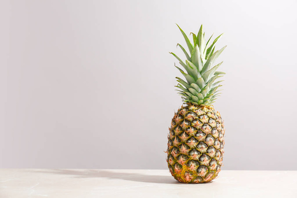 Fresh pineapple on table against grey wall - Zdjęcie, obraz