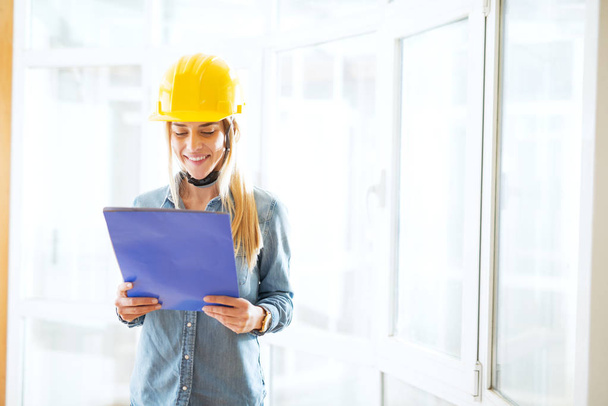 young happy female engineer with yellow helmet looking at blueprint - Foto, Bild