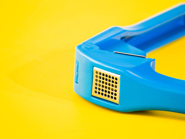 鮮やかなネオン黄色切削ボード背景無料色を並置の偉大なイメージを作る明るい青いプラスチック ガーリック プレス キッチン用品ツールの写真を閉じる. - 写真・画像
