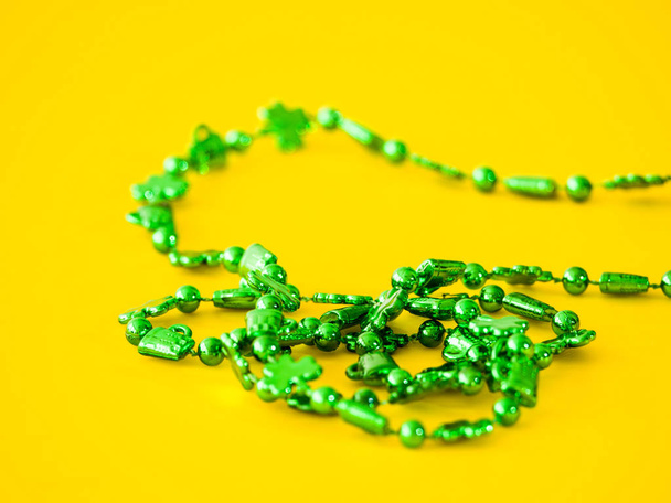 Closeup photograph of a strand of beads from a st. patricks day plastic green necklace with clovers on a bright saturated yellow background creating a beautiful juxtaposed colorful background ima - Photo, Image