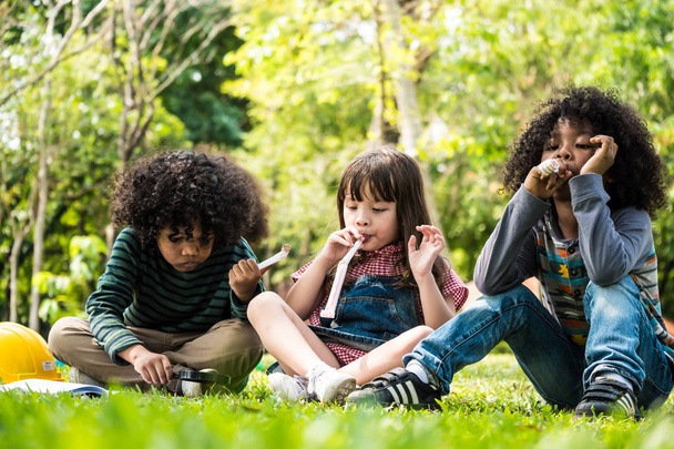 Niños jugando juntos mientras están sentados sobre hierba verde en un parque
 - Foto, Imagen