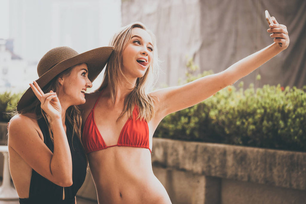 Δύο όμορφα κορίτσια έχουν τη διασκέδαση λήψη φωτογραφιών selfie με έξυπνο τηλέφωνο φωτογραφικών μηχανών στην πισίνα - Φωτογραφία, εικόνα