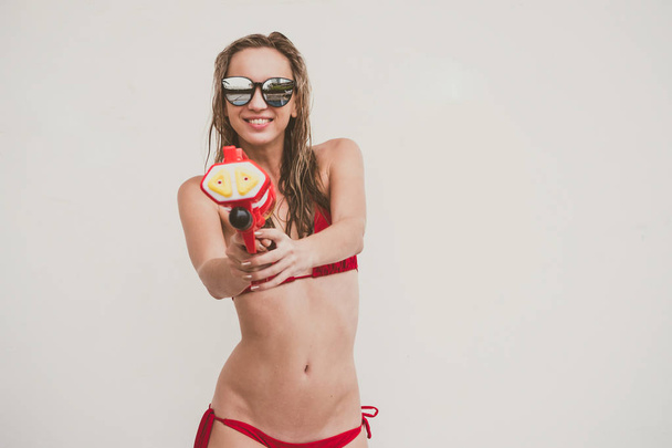 Atractiva joven en bikini rojo sosteniendo pistola de agua sobre fondo blanco - Foto, imagen