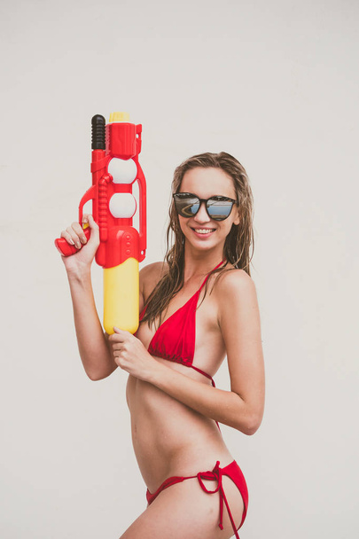 Aantrekkelijke jonge vrouw in de rode bikini met waterpistool op witte achtergrond - Foto, afbeelding