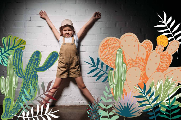 little child in safari costume standing at white wall with cactuses illustration - Photo, Image
