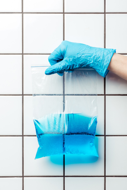 cropped image of woman in blue rubber glove holding ziplock plastic bag with blue water, earth day concept - Foto, imagen