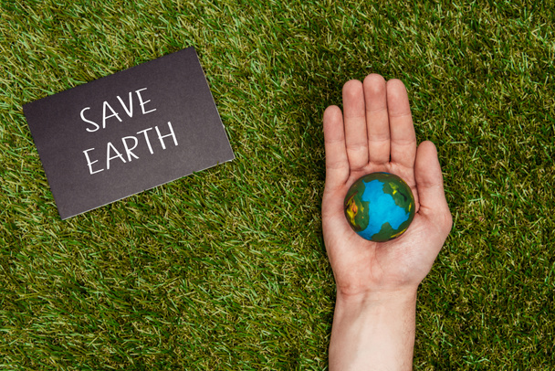 cropped image of man holding earth model in hand with sign save earth on green grass, earth day concept - Fotoğraf, Görsel