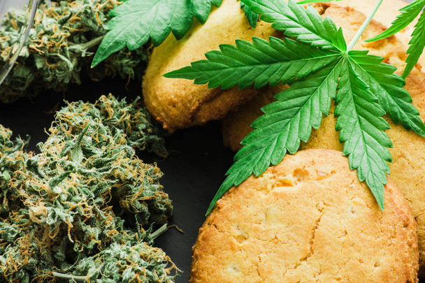 CBD Cookies with cannabis and buds of marijuana on the table. A can of cannabis buds Concept of cooking with cannabis herb. Treatment of medical marijuana for use in food, On a black background - Photo, Image