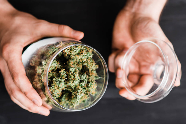 Une boîte ouverte avec des bourgeons de cannabis dans les mains d'un homme. Le concept de marijuana légale est l'herbe médicale. Sur fond noir. Vue du dessus
 - Photo, image