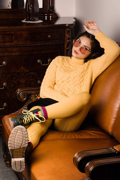 Приваблива молода дівчина сидить на красивому шкіряному дивані
 - Фото, зображення