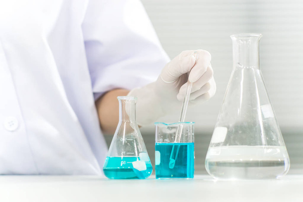 Fles in wetenschapper met druppelende chemische vloeistof voor het testen van buizen, wetenschappelijk en medisch onderzoeks- en ontwikkelingsconcept - Foto, afbeelding