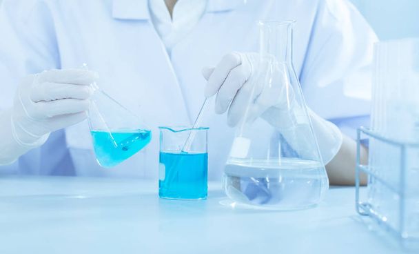 Flask in scientist hand with dropping chemical liquid to test tubes, science and medical research and development concept - Photo, Image