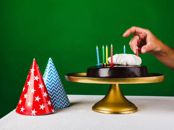 Рука жінки прикрасила шоколадний торт з шістьма свічками на золоті
 - Фото, зображення