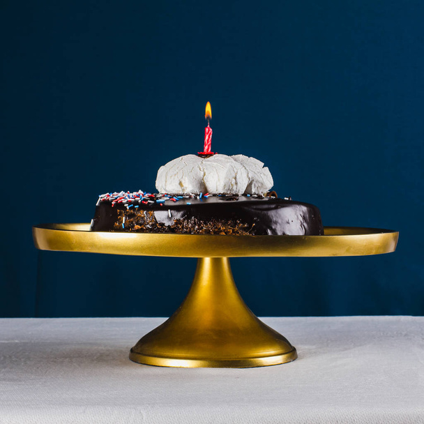 Red candle in chocolate cake  on golden tray and dark blue backg - Valokuva, kuva