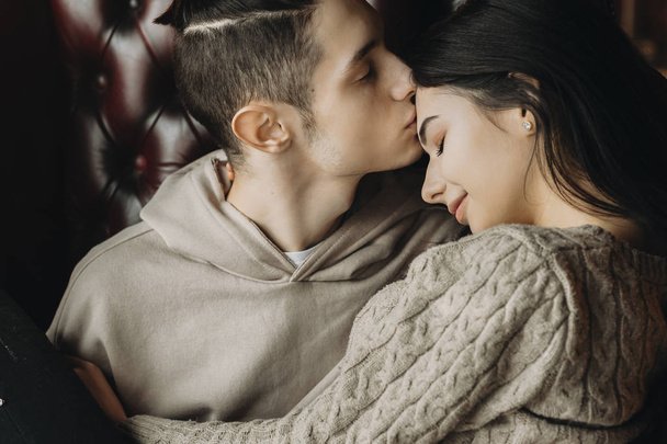 Doux jeune couple rester sur un canapé tandis que le garçon embrasse son lo
 - Photo, image