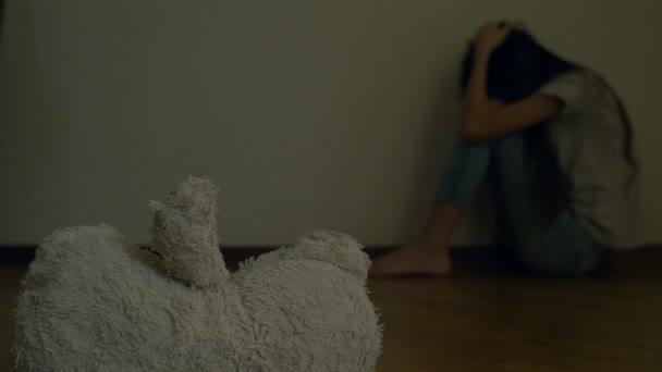 een wanhopig kind in depressie zit op de muur van zijn kamer, probeert om te proberen van zelfmoord. ernaast is een verlaten zacht stuk speelgoed. 4k, slow-motion. - Video