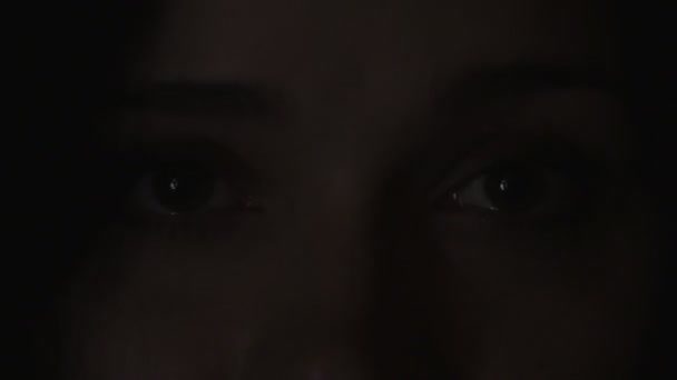 Nahaufnahme der Augen einer jungen Frau, die sich ein Video oder einen Film auf dem Fernseher oder einem Computermonitor ansieht. Spiegelung auf ihrem Gesicht - Filmmaterial, Video