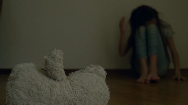 zoufalé dítě v deprese sedí na zdi svého pokoje, snaží se pokusí o sebevraždu. vedle něj je opuštěné Plyšová hračka. 4k, pomalý pohyb. - Záběry, video