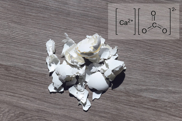 Tojáshéj az asztalon, a háttérben az a kémiai név kalcium-karbonátot. Kalcium-karbonát, ásványi anyagok, formájában természetesen megtalálható a tojáshéj részét képezi. A mindennapi életben használt lúgosítják a talaj, Kertészet. - Fotó, kép