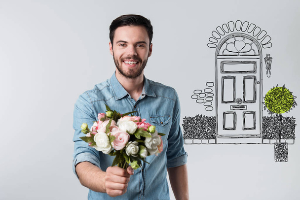 Beautiful flowers. Handsome young kind man holding a beautiful bouquet of flowers while making a romantic surprise for his girlfriend - Photo, Image