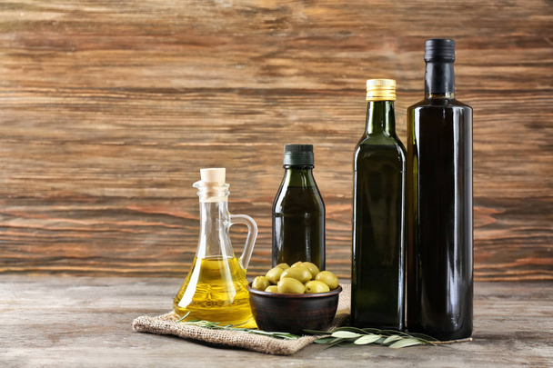 Композиція з оливковою олією в пляшках і глечику на дерев'яному фоні
 - Фото, зображення