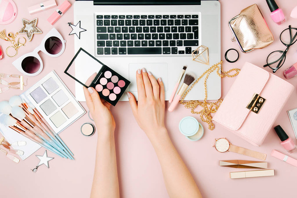 Cropped view of female fashion blogger working with laptop on workspace with accessories, cosmetics products. - Fotó, kép