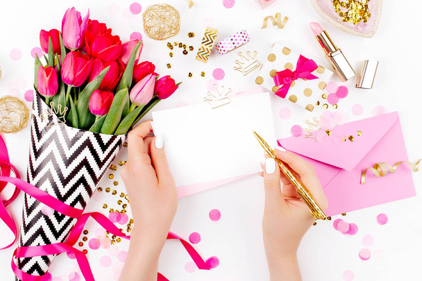 Female hands holding card with pen and pink and gold styled desk with florals.  - Foto, afbeelding