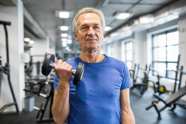 Strong senior man holding dumbbell in gym - 写真・画像