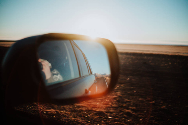 Kijken door een terug spiegel van een auto in IJsland bij zonsondergang. - Foto, afbeelding