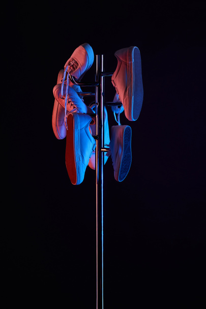 various shoes hanging on coat rack under toned light isolated on black - Foto, immagini