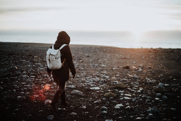 Ένα άτομο που περπατάει σε μια παραλία με μαύρη άμμο στην Ισλανδία στο ηλιοβασίλεμα - Φωτογραφία, εικόνα