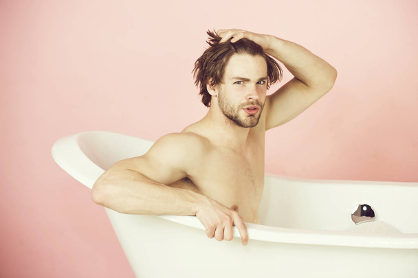 handsome young man with muscular body sitting in white bathtub - 写真・画像