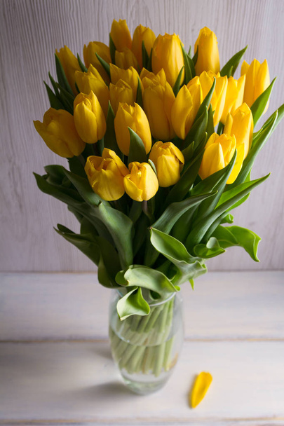 Bouquet of spring tulips flowers in vase on white wooden background. Yellow tulips - Foto, immagini